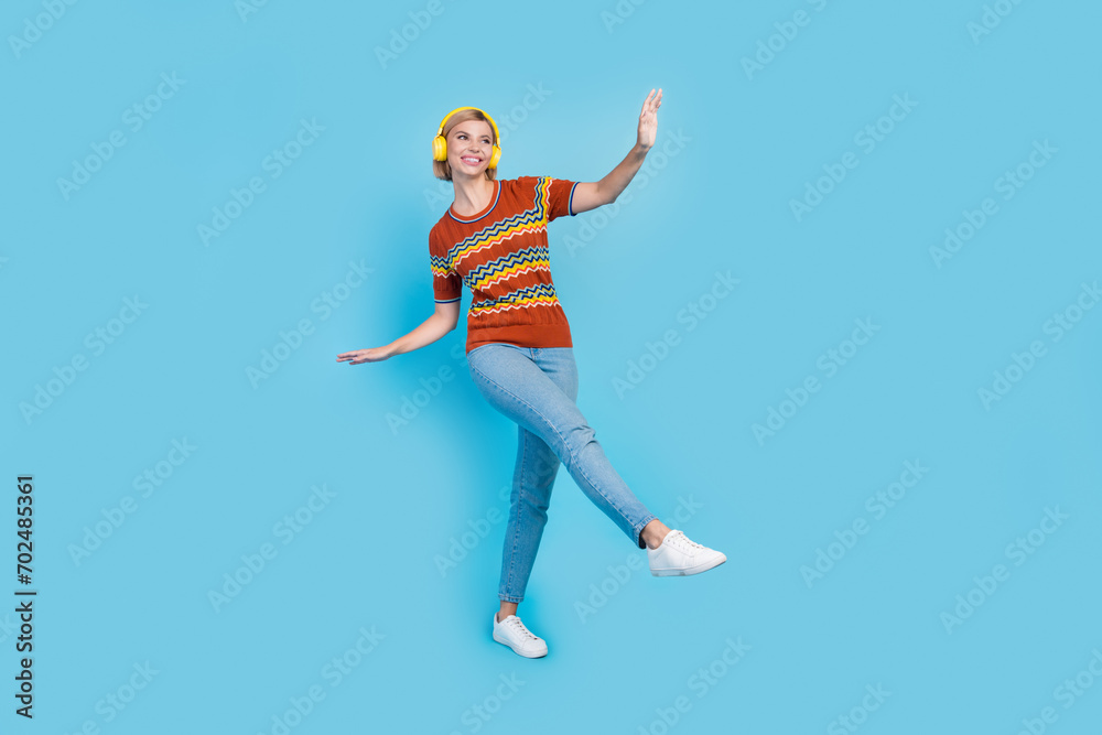 Full length photo of good mood girl wear strited t-shirt in headphones dancing look at sale empty space isolated on blue color background Full length photo of good mood girl wear strited t-shirt in headphones dancing look at sale empty space isolated on blue color background