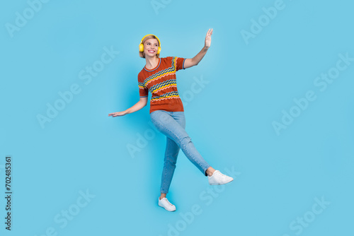 Full length photo of good mood girl wear strited t-shirt in headphones dancing look at sale empty space isolated on blue color background