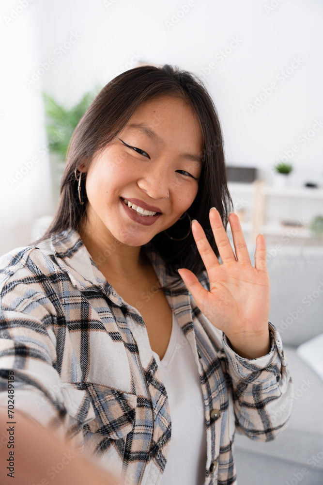 Vertical photo of a Chinese woman greeting at camera while taking selfie from home Vertical photo of a Chinese woman greeting at camera while taking selfie from home