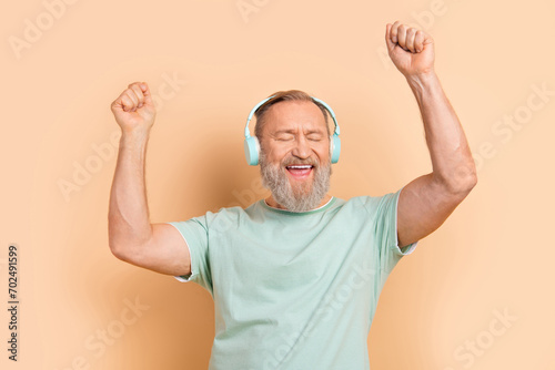 Photo of cheerful positive glad man wear trendy cyan outfit raised hands have fun isolated on beige color background