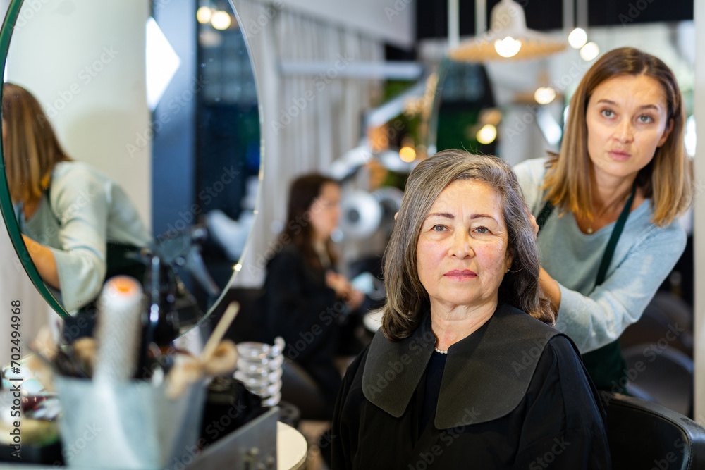 Φωτογραφία Pleasant elderly silver haired female client sitting in chair while discussing haircut with professional hairdresser