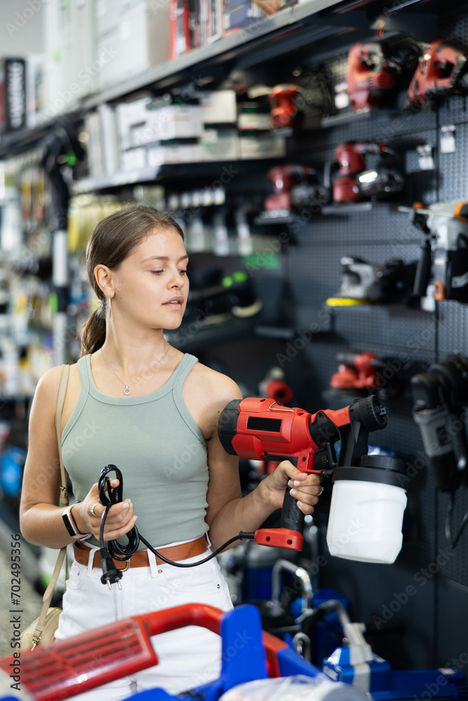Woman chooses and buys paint spray gun in a hardware store
