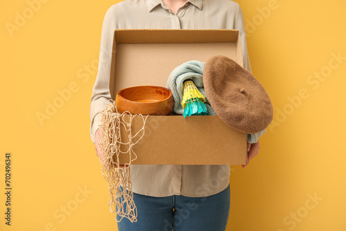 Woman holding box of unwanted stuff for yard sale on yellow background photo
