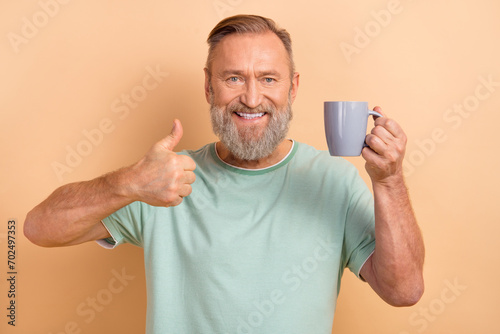Photo of positive satisfied man wear trendy clothes demonstrate thumb up nice feedback isolated on beige color background