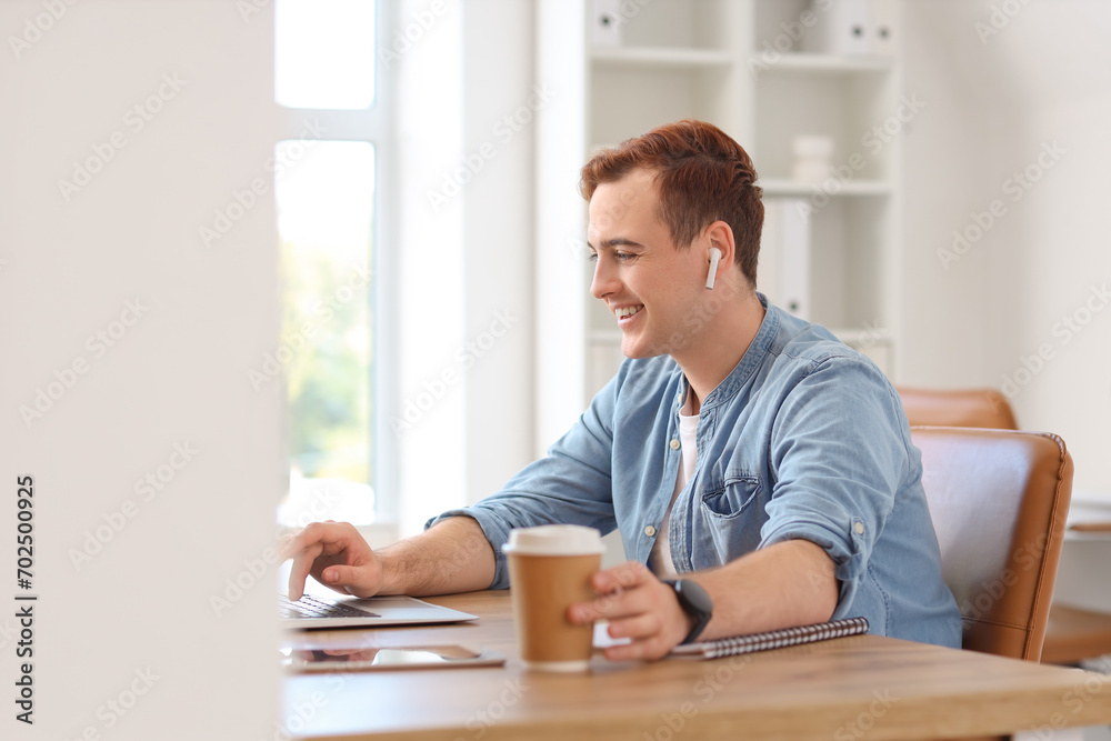 Young businessman with cup of coffee working at table in office
