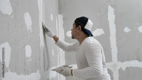 Plasterwork and wall painting preparation. Asian male applying filling drywall patch.