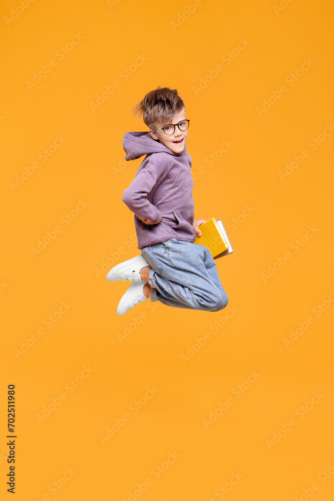 Cute schoolboy with books jumping on orange background, space for text Cute schoolboy with books jumping on orange background, space for text