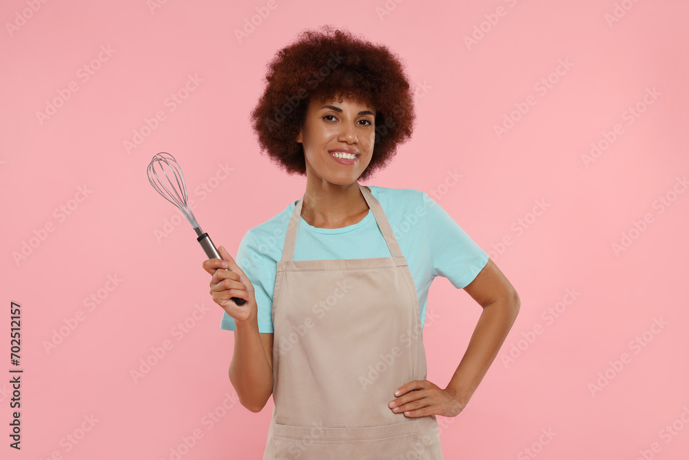Happy young woman in apron holding whisk on pink background Happy young woman in apron holding whisk on pink background