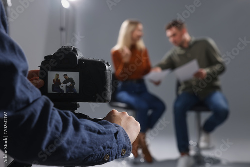 Casting call. Man and woman performing while camera operator filming them against grey background in studio, selective focus photo