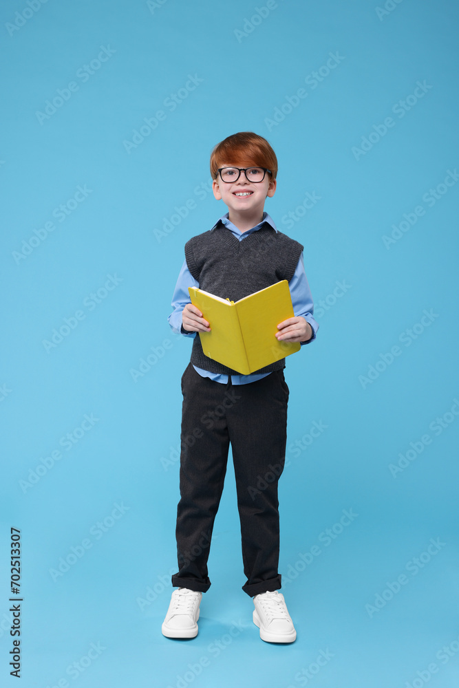Smiling schoolboy in glasses with book on light blue background Smiling schoolboy in glasses with book on light blue background