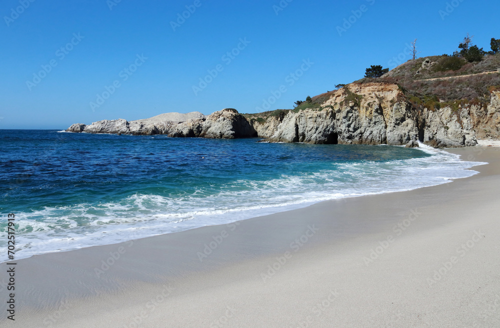 Shoreline and sandy beach. Gray sand, blue bay water and blue clear sky.