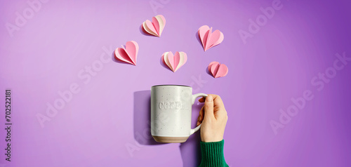 Female hand holding a mug with paper craft hearts - flat lay photo