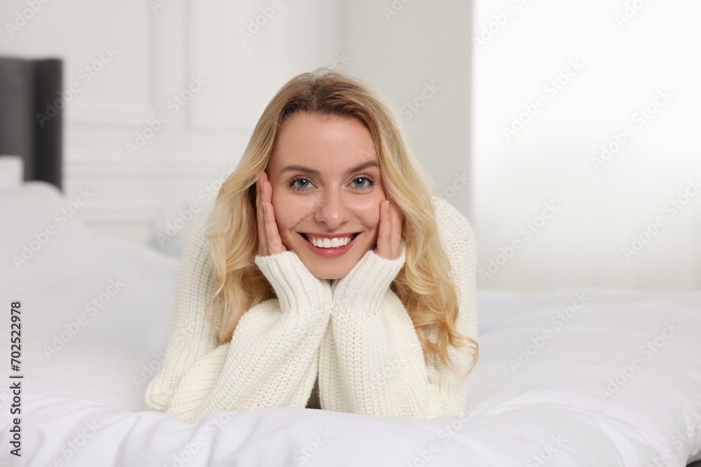 Happy woman in stylish warm sweater lying on bed indoors Happy woman in stylish warm sweater lying on bed indoors