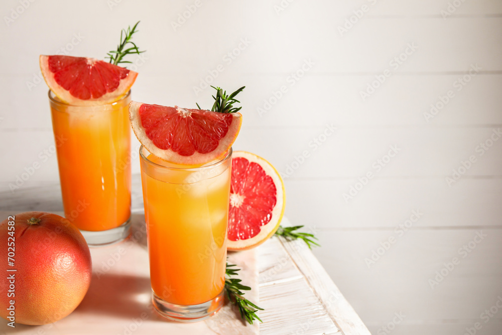 Tasty grapefruit drink with ice in glasses, rosemary and fresh fruits on light wooden table. Space for text Tasty grapefruit drink with ice in glasses, rosemary and fresh fruits on light wooden table. Space for text