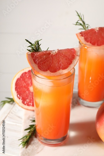 Tasty grapefruit drink with ice in glasses, rosemary and fresh fruits on light table