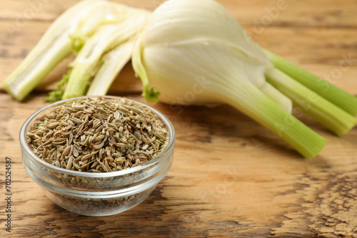 Fennel seeds in bowl and fresh vegetables on wooden table, closeup