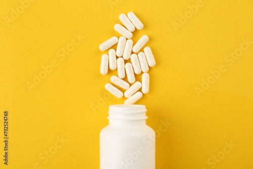 Bottle and vitamin capsules on yellow background, top view photo