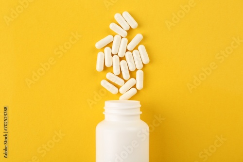 Bottle and vitamin capsules on yellow background, top view