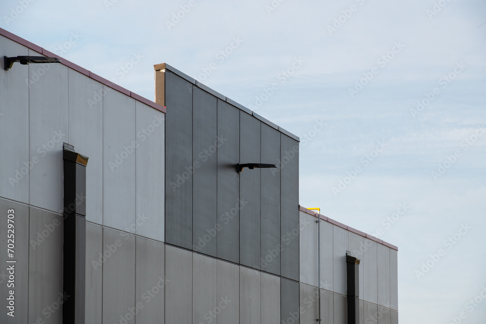 Commercial external vertical metal composite panels on a large building with clouds in the background. The durable metal composite panels are various shades of grey color on the modern building. Commercial external vertical metal composite panels on a large building with clouds in the background. The durable metal composite panels are various shades of grey color on the modern building.