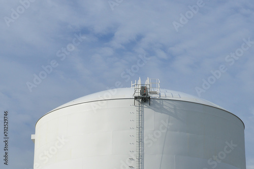 Obraz na plátně The exterior of a tall white metal industrial cylinder tower with a ladder on the side of the liquid crude petroleum refinery storage container at an energy plant