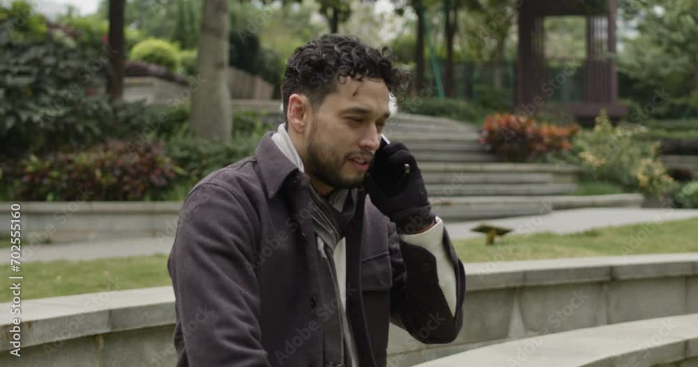 Push in on handsome Hispanic ethnicity man talks positively, confident on the phone outdoors in the park. Push in on handsome Hispanic ethnicity man talks positively, confident on the phone outdoors in the park.