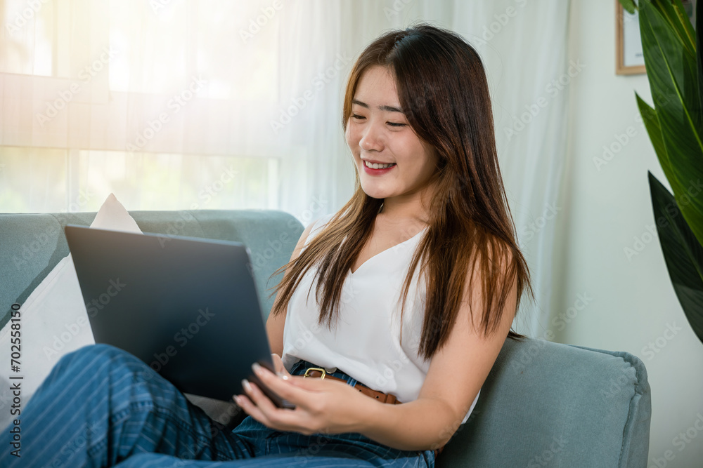 Happy woman browsing through the internet during free time on laptop computer, Female smiling sit on sofa using laptop in living room at home, girl shopping or chatting online in social media network Happy woman browsing through the internet during free time on laptop computer, Female smiling sit on sofa using laptop in living room at home, girl shopping or chatting online in social media network