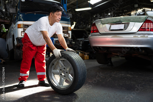 mechanic holding and pushing a tire for fixing in garage © offsuperphoto