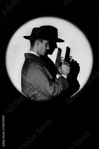 A dark silhouette of a male detective in a coat and hat with a gun in his hands in the noir style. A dramatic portrait in the style of detective films of the 1950s. The silhouette of a spy in a circle