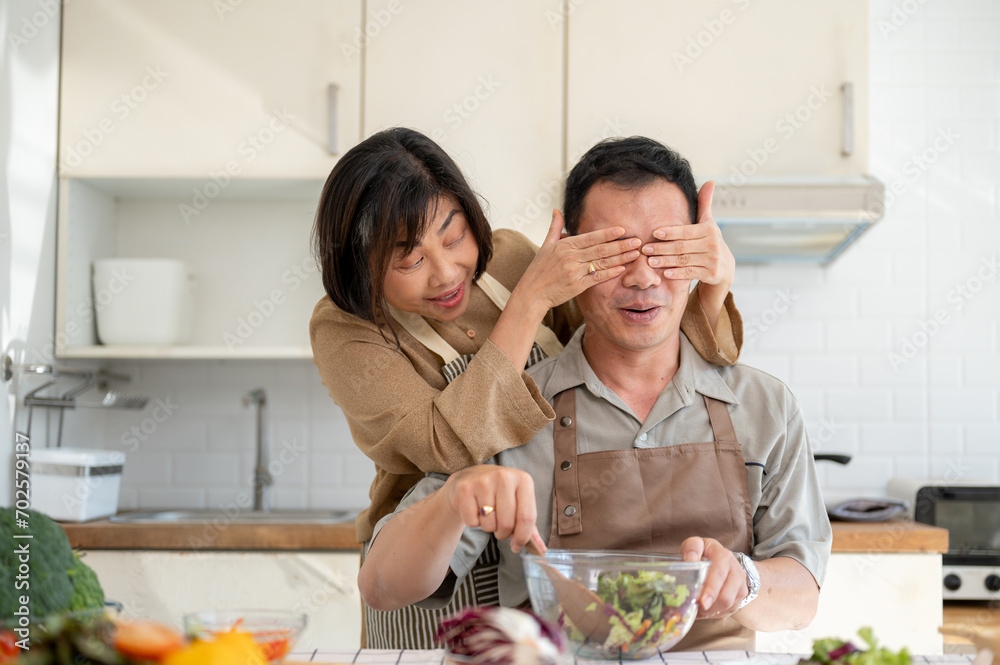 A happy, playful Asian wife is teasing her husband while he is cooking. Peek a boo