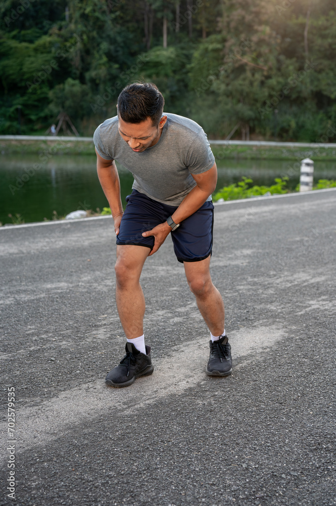 An Asian man in sportswear is feeling hurt on his knee after a long run. intense workout
