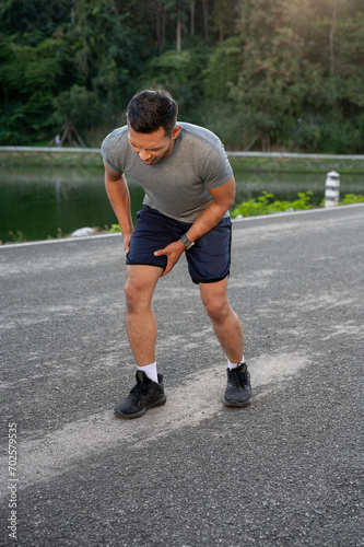 An Asian man in sportswear is feeling hurt on his knee after a long run. intense workout