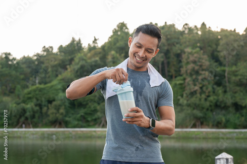Fotografía A happy, strong Asian man in sportswear is drinking a protein shake after a long run outdoors