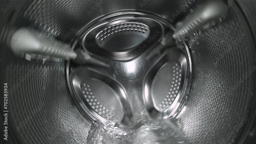 Inside view of the washing machine drum, close-up of the stainless steel drum during the spin cycle, splashing water and foam.