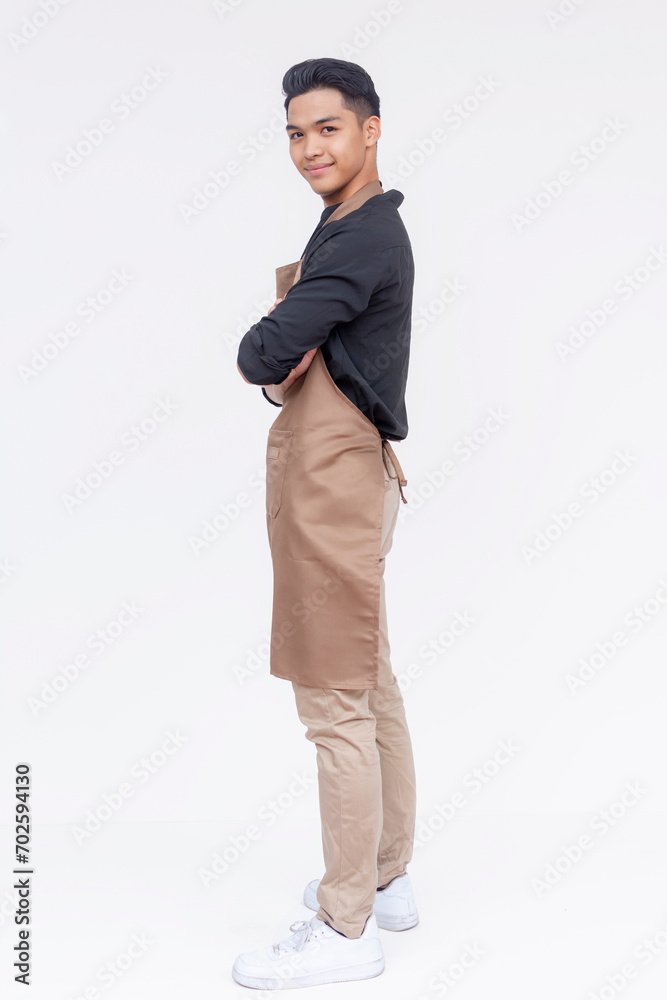 Naklejka premium A handsome and young asian barista, arms crossed and standing. Side view full body studio shot, with white background.