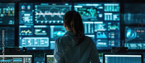 Rear view of female data scientist analyzing information on big digital screen in monitoring office. Diverse employees working for big data company. © 2rogan