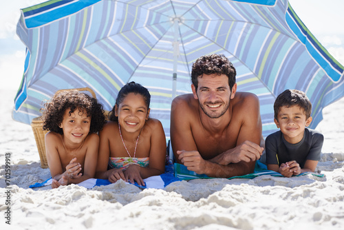 Father, children and family on beach, happy in portrait for summer vacation with parasol, bonding and love. People outdoor for holiday in Brazil with sand and sun, travel and adventure together #702599913
