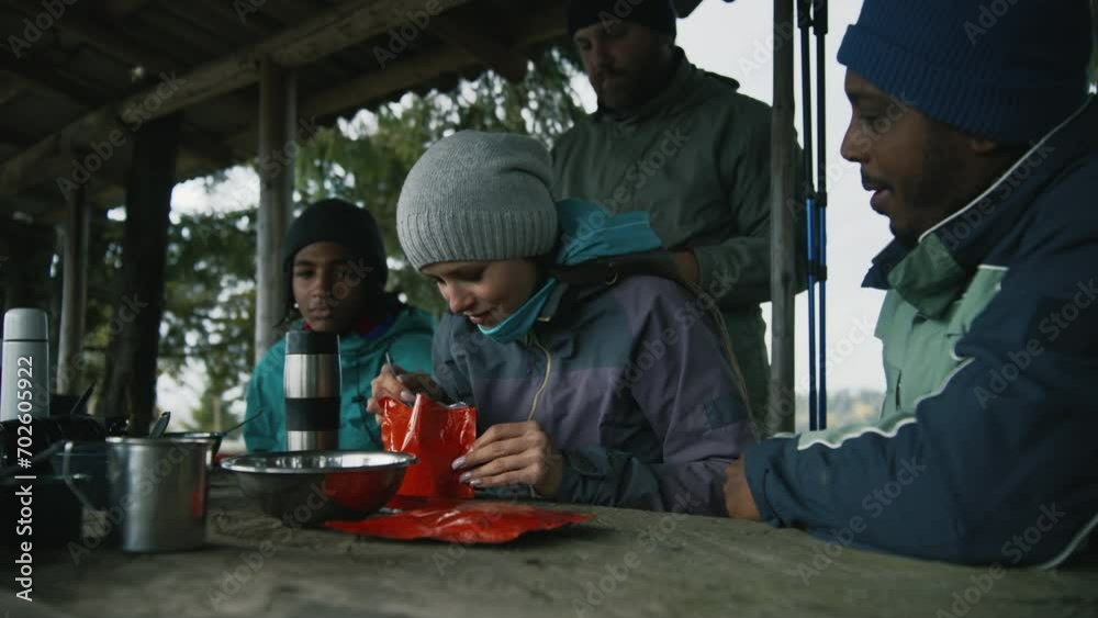 Adult African American man opens doy pack for his wife. Multiethnic tourist family eat hiking food together. Group of travelers or hikers rest in gazebo after expedition or trek in the mountains. Adult African American man opens doy pack for his wife. Multiethnic tourist family eat hiking food together. Group of travelers or hikers rest in gazebo after expedition or trek in the mountains.