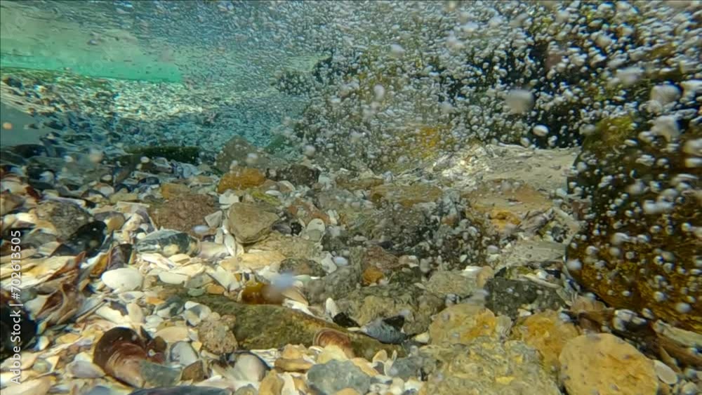 Slow motion, Turbulent stream of water with air bubbles at mouth of river flowing into the sea, seabed covered with small stones and shells, Close up