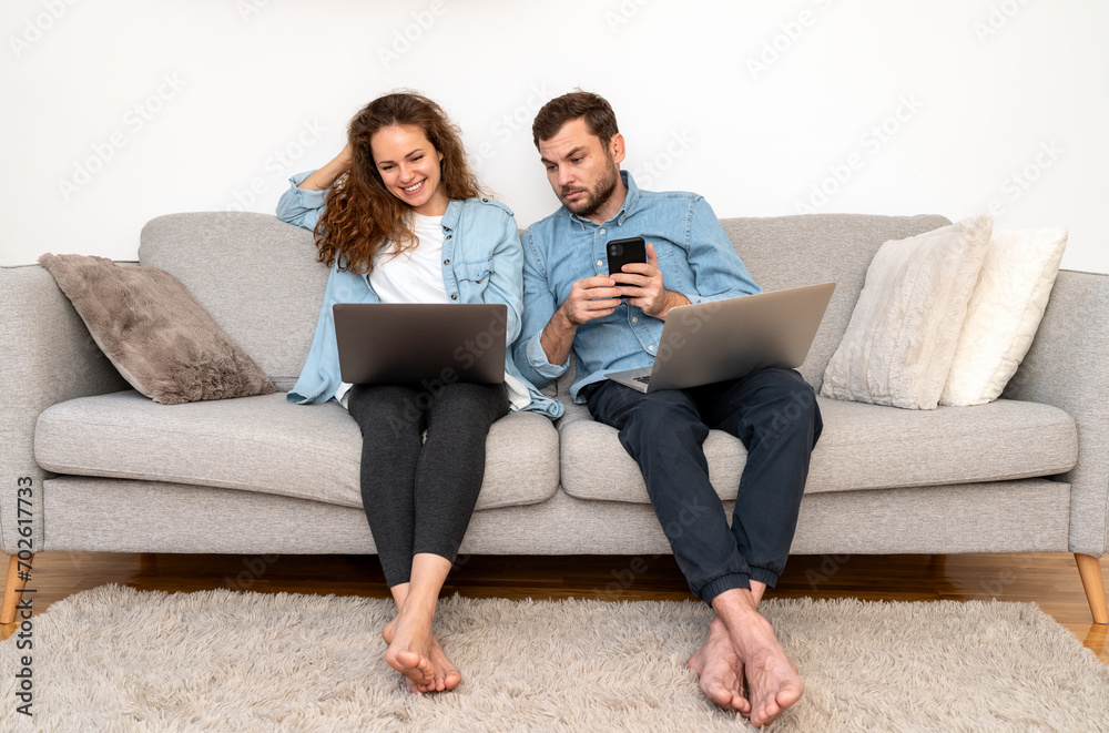 Two people woman and man sitting on sofa at home and use their digital devices.