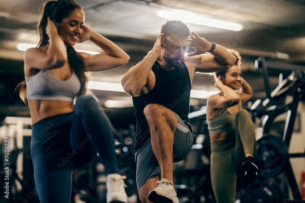 Group of friends doing high knees exercise on a gym with male coach.