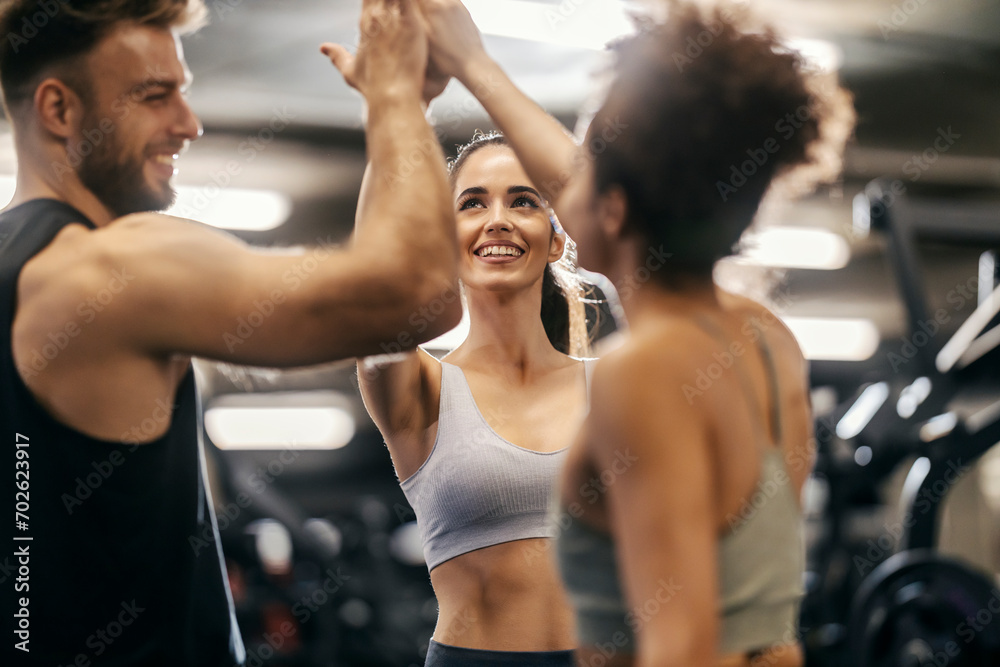 Group of fitness friends giving high five for achievement in a gym.