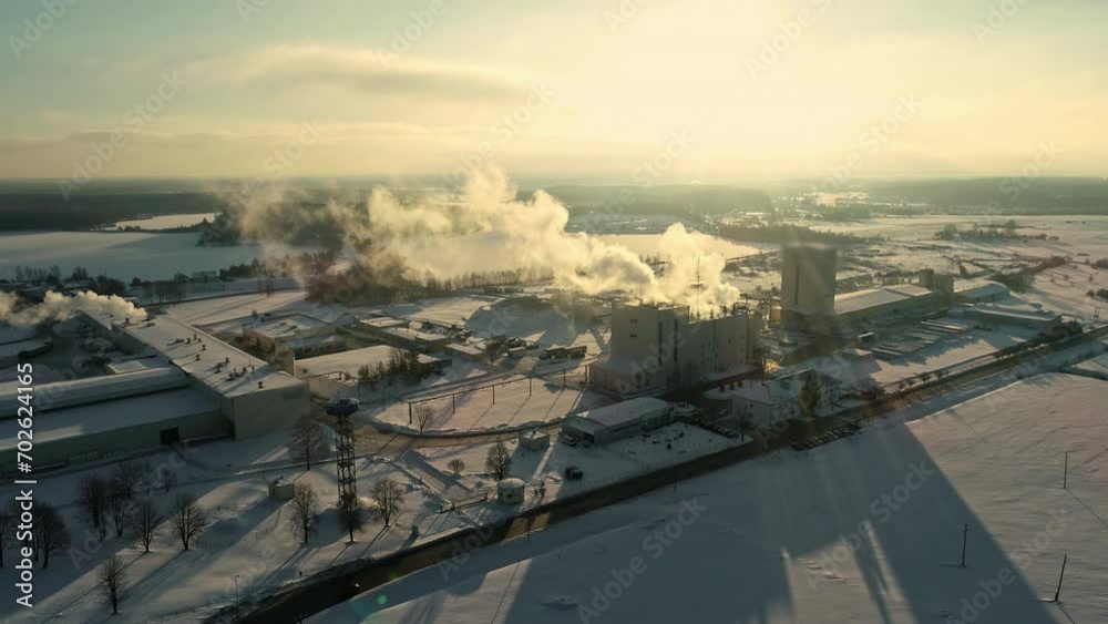 Backlit smoke rising from industrial building covered in snow backlit by sun in winter Backlit smoke rising from industrial building covered in snow backlit by sun in winter