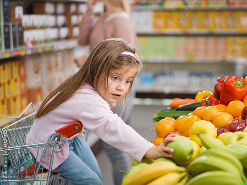 Cute girl taking a fruit in the produce section while her mother is distracted