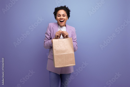 young pretty cute hispanic business woman with curly hair in a lilac jacket received delivery in an eco-friendly paper craft bag