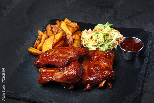 Barbecue pork ribs with baked potatoes and fresh cabbage salad on a black background.