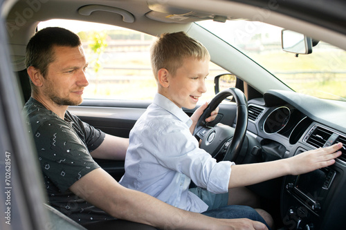 Dad and happy son in the front seat of a car driving a car. The boy holds the steering wheel.