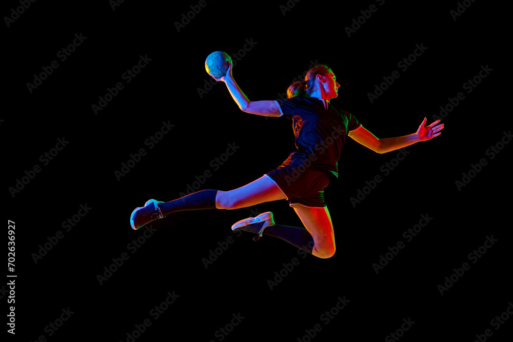 Determined female athlete practicing handball moves with concentration and dedication against black background in neon light. Concept of sport and action, dynamic, victory, championship, ad.