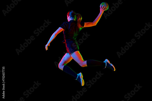 Fit young woman engaged in intense handball training, perfecting her throwing and catching abilities against black background in neon light, filter. Concept of sport, hobby, dynamic, championship. Ad © Lustre