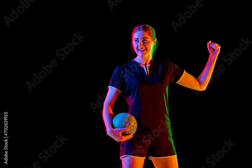 Young woman, professional handball athlete happy because she scored perfect decisive goal against black background in mixed neon light. Concept of professional sport, championship 2024, victory. Ad