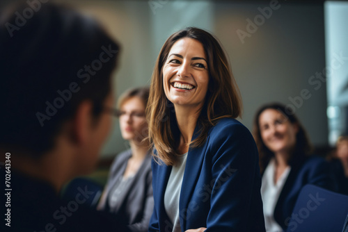 A woman in a group smiling at a woman meeting at a conference room, in the style of artistic reportage, back button focus, light amber and indigo, viennese actionism, focus on joints/connections, shap photo